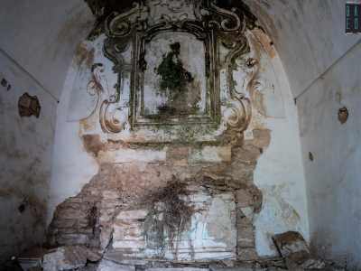 Entriamo prima nella cappella, che originariamente era arricchita da un dipinto della Madonna di cui oggi non resta che la cornice in gesso